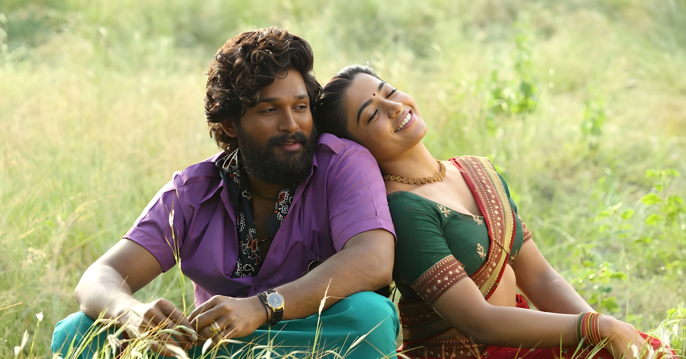 Allu Arjun as Pushpa Raj and Rashmika Mandanna as Srivalli sitting in a lush green field from Pushpa movie..